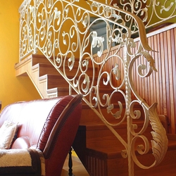 A hand wrought iron interior staircase railing - A white railing with gold-green patina