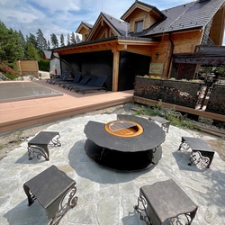 Hand-forged garden chairs as part of a multifunctional fireplace with a grill and storage space for wood