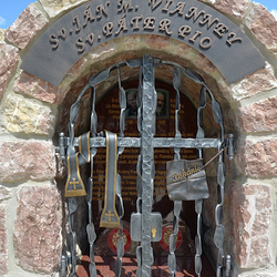 Kovaný pamätník svätých s atribútmi na mrežiach. Sv. Ján M. Vianney - štóla, Sv. Páter Pio - list s nápisom Pokánie